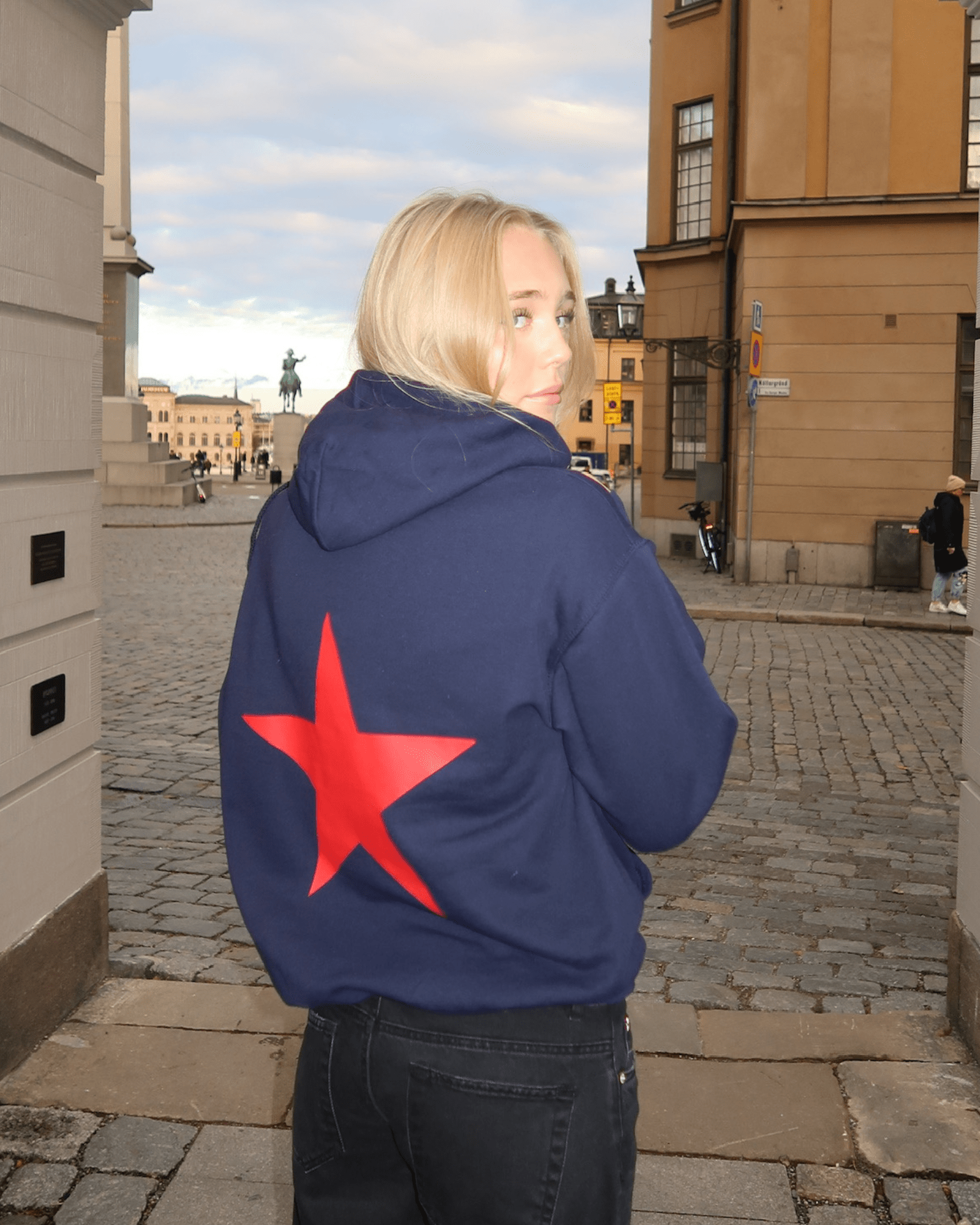 Navy hoodie med stort rødt stjerneprint på ryggen, båret af en kvinde på gaden