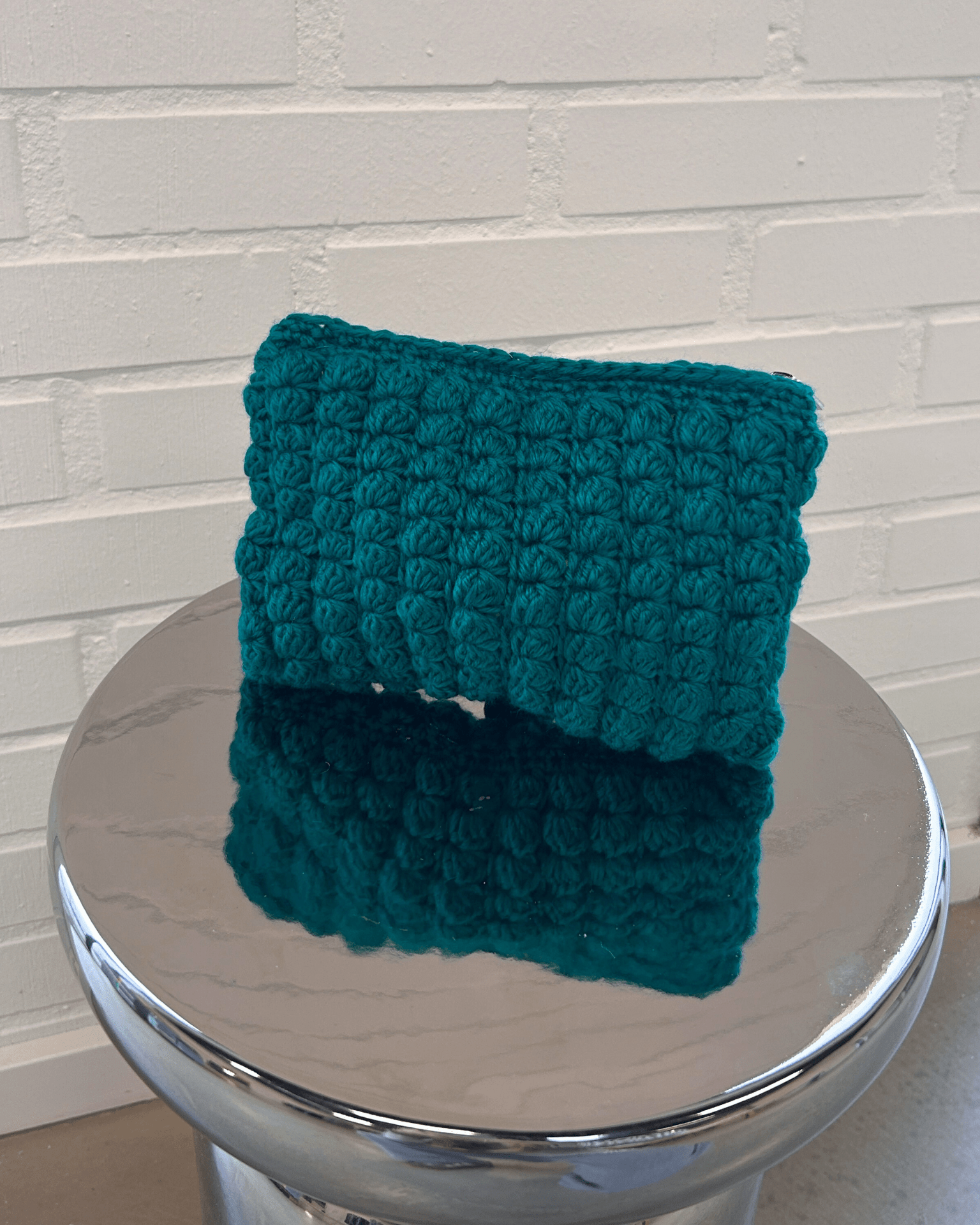 Grøn hæklet clutch i boblemønster på et blankt metalbord