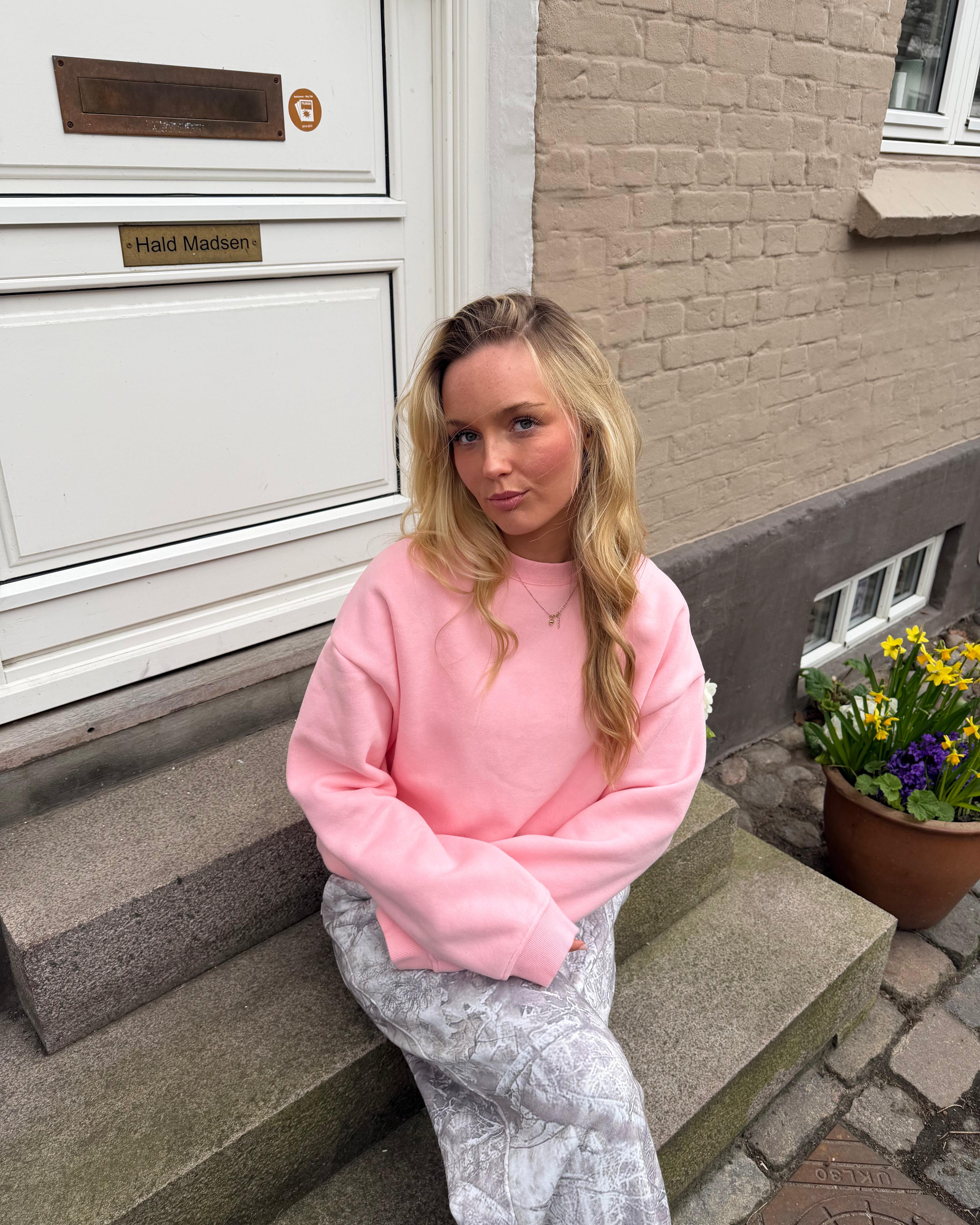 Lyserød oversized sweatshirt i bomuld på en kvinde, der sidder på en trappe