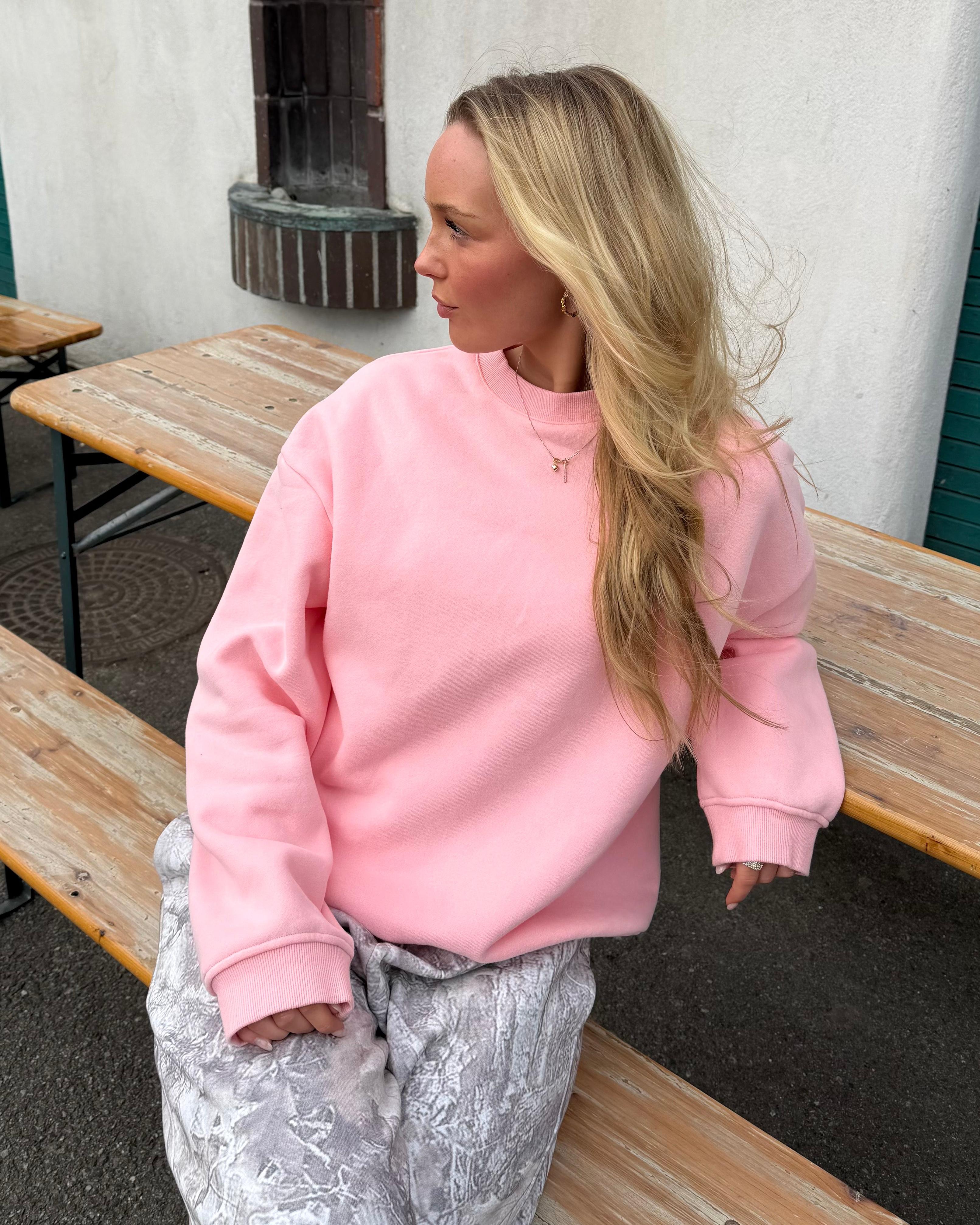 Lyserød oversized sweatshirt i bomuld på blond model, der sidder ved et træbord