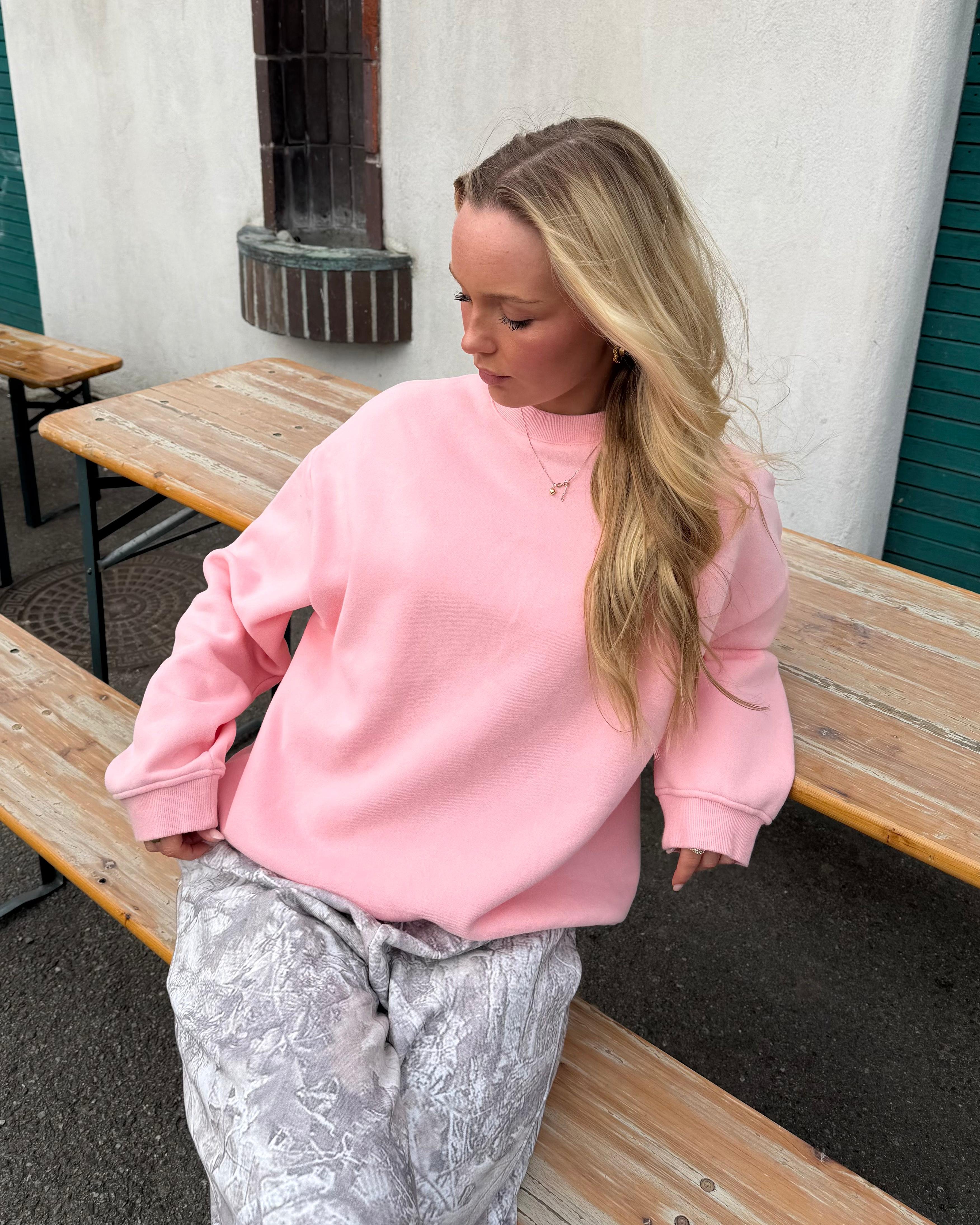 Lyserød oversized sweatshirt i bomuld på model, der sidder ved et træbord