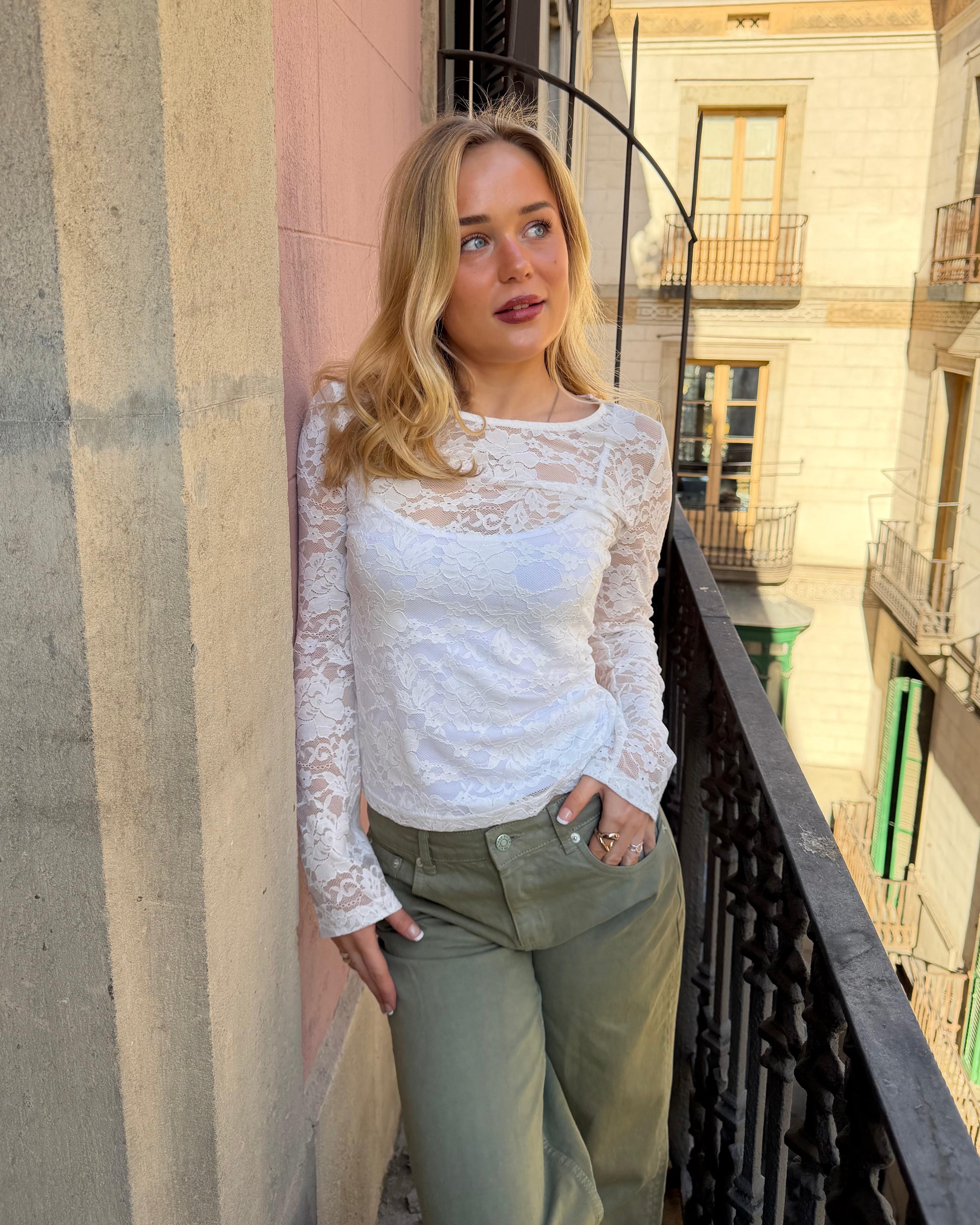 Hvid langærmet Alix blondetop i tætsiddende pasform vist på model på en altan