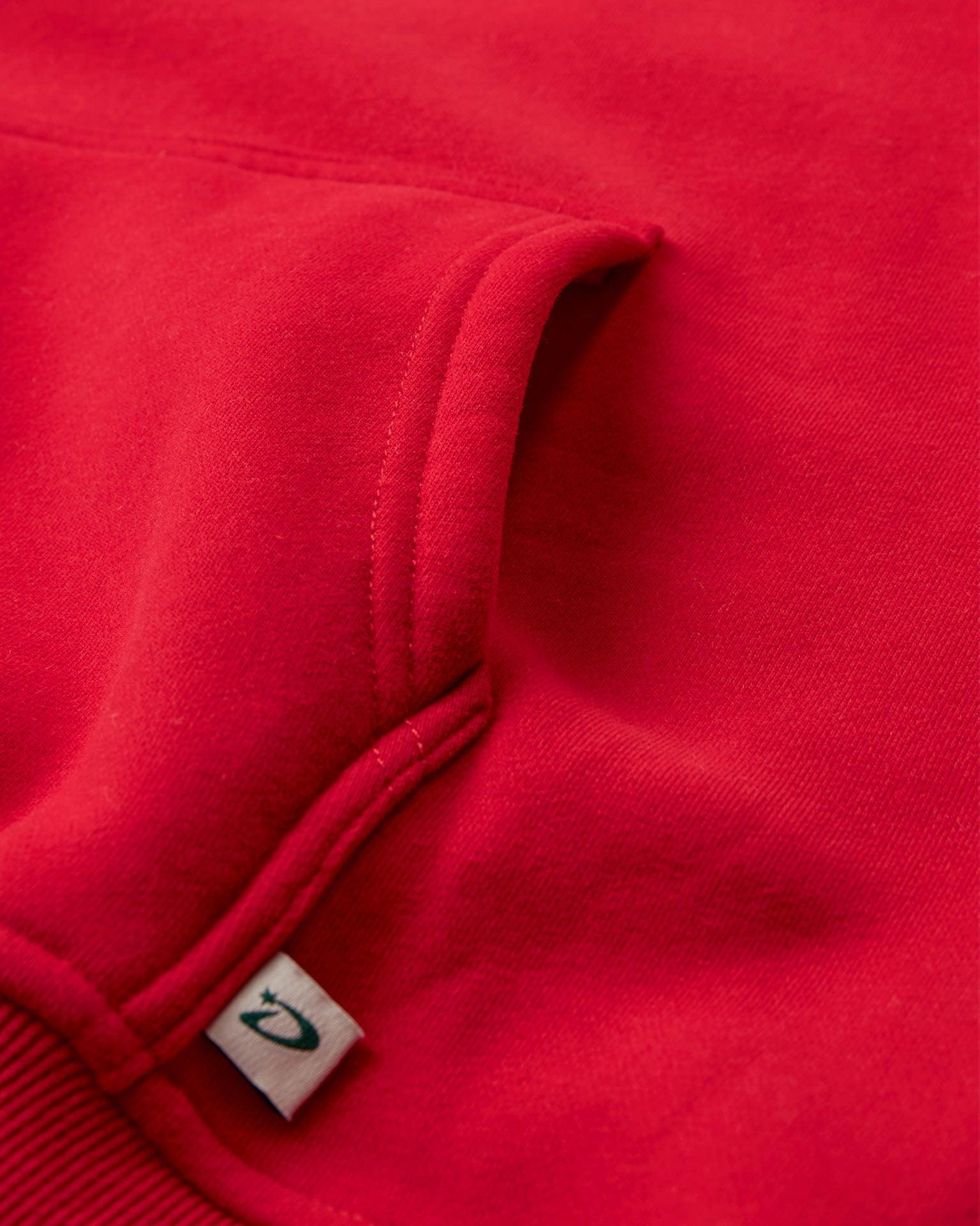 Nærbillede af rød oversized bomuldshoodie med kængurulomme og lille logo-mærke